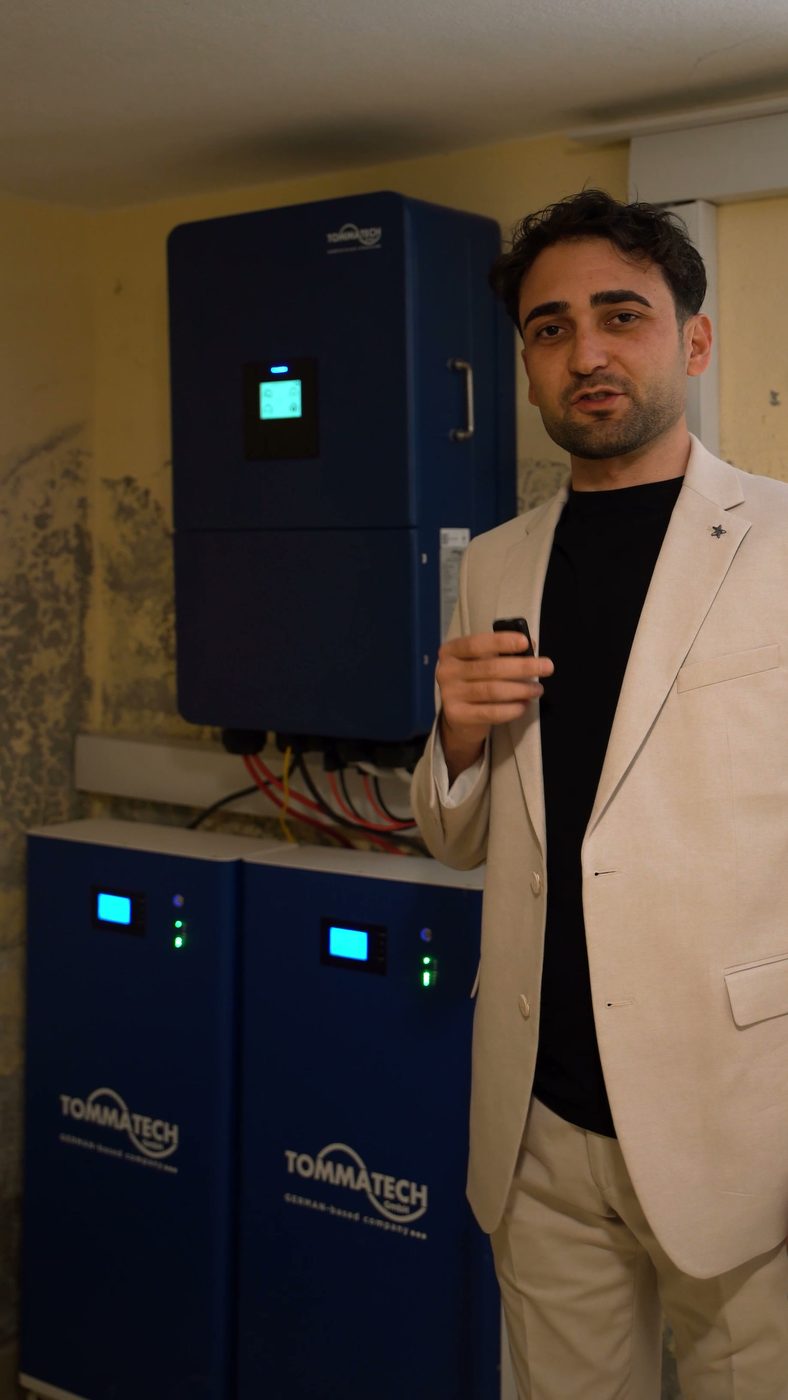 Solartep'ten Furkan Bey, duvardaki 15 kW Tommatech inverter ve dört lityum bataryanın önünde